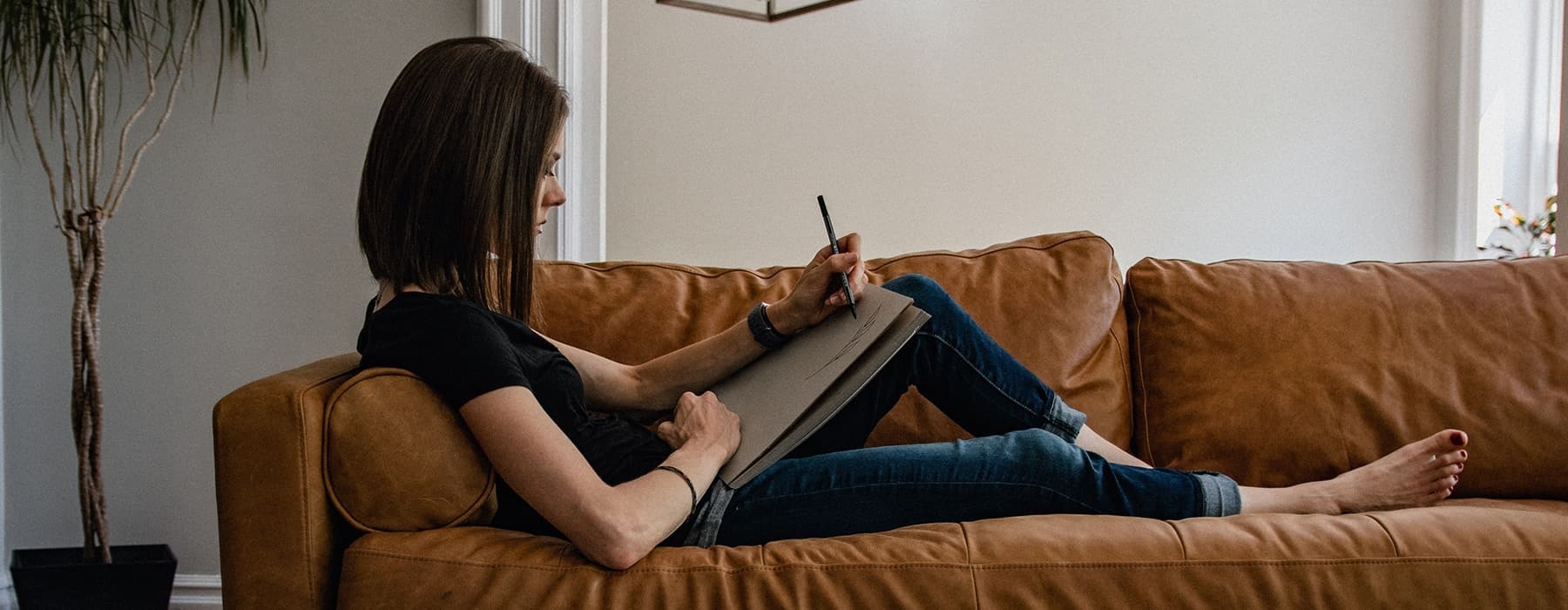 lifestyle image of a woman laying and working on a brown couch